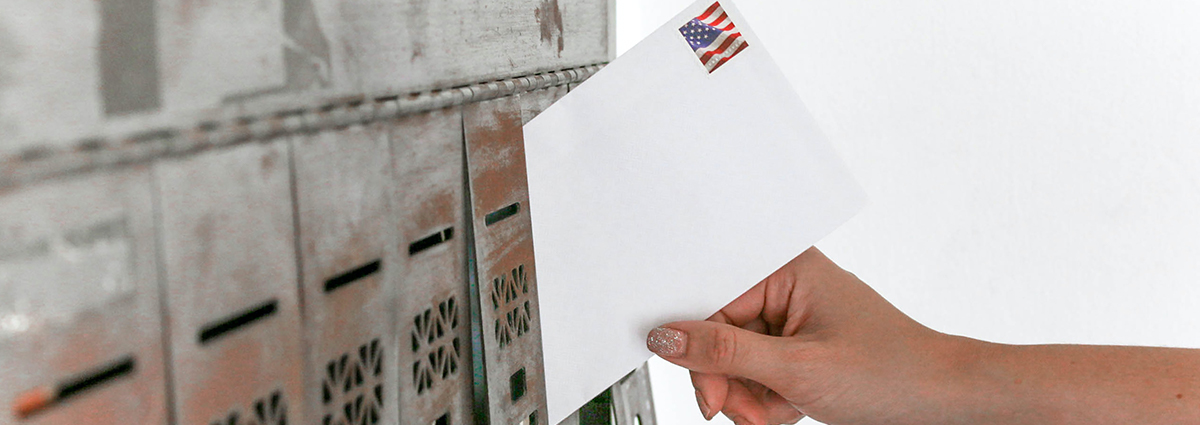 A hand slides an envelope into a mailbox.
