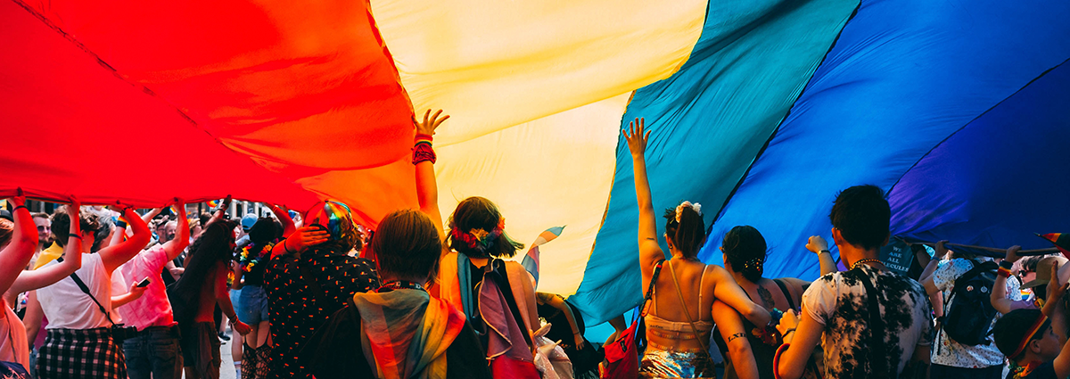 People stand under a giant rainbow flag.
