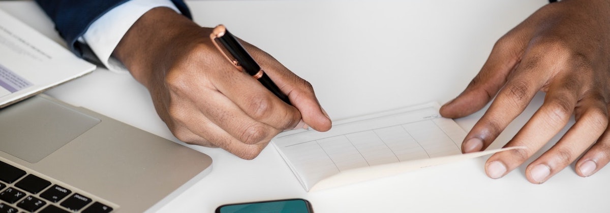 Person signs a paper in pen while a computer sits to the side