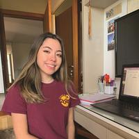 Woman sitting at a desk with a computer while wearing a maroon Class of 2020 shirt
