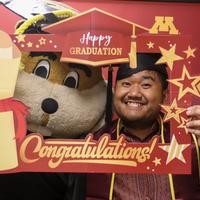Yuth in a graduation cap and gown with Goldy Gopher 