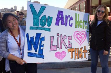 Two ISSS staff members holding a sign saying "You are here! We like that"